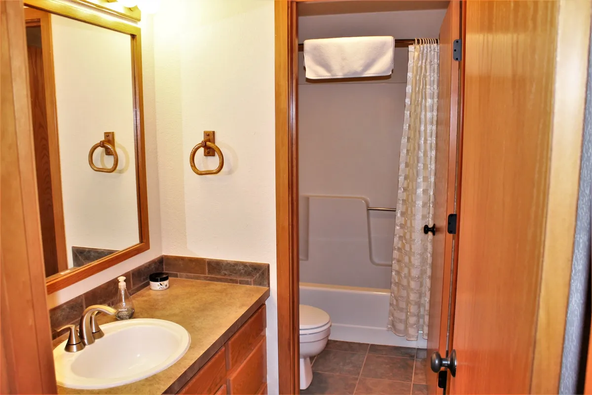 A bright, functional bathroom featuring a sink with mirror, towel rack, shower curtain, and toilet. The decor is simple but inviting, supporting both self-care and practical routines.