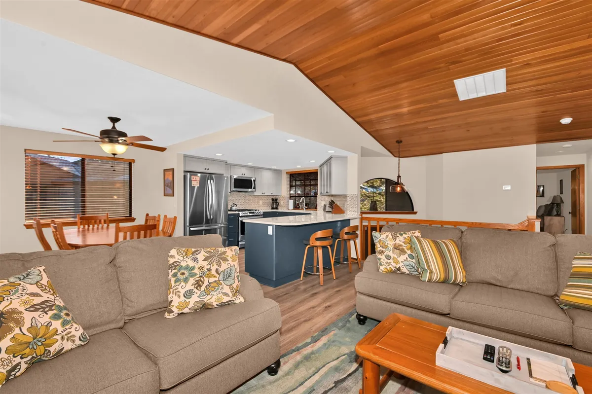 A bright, inviting space showcasing comfortable sofas with decorative pillows, an adjacent dining area with a wooden table, and a modern kitchen complete with stainless steel appliances. The room exudes an atmosphere of relaxation and togetherness, perfect for casual dining or entertaining guests.