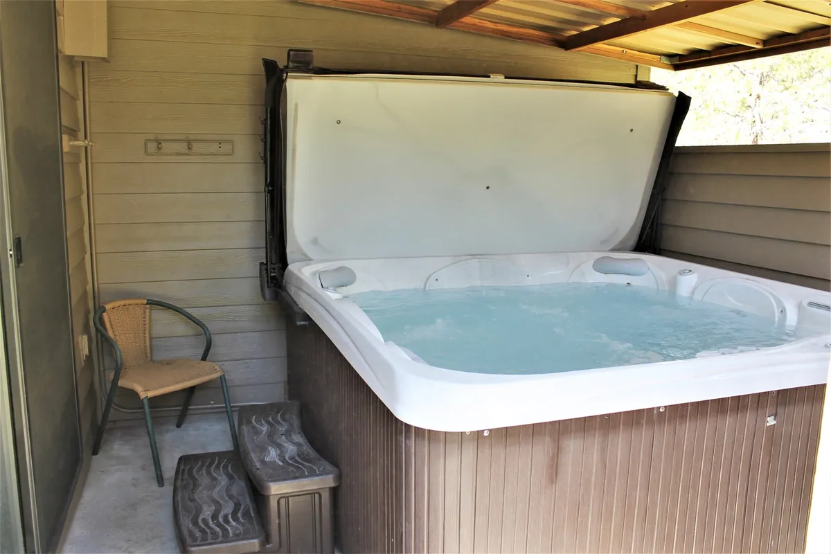 An inviting indoor hot tub area featuring a spacious tub with clean tile surroundings, a comfortable chair nearby, and steps leading into the tub. Soft lighting and an uncluttered setting create a tranquil mood, hinting at the perfect spot for relaxing soaks after a day of adventure.