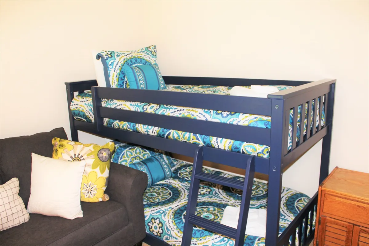 A playful bunk room furnished with a sturdy bunk bed dressed in colorful bedding, a comfortable couch with pillows, and a wooden dresser. The ambiance is cheerful and family-friendly, perfect for children or young guests.