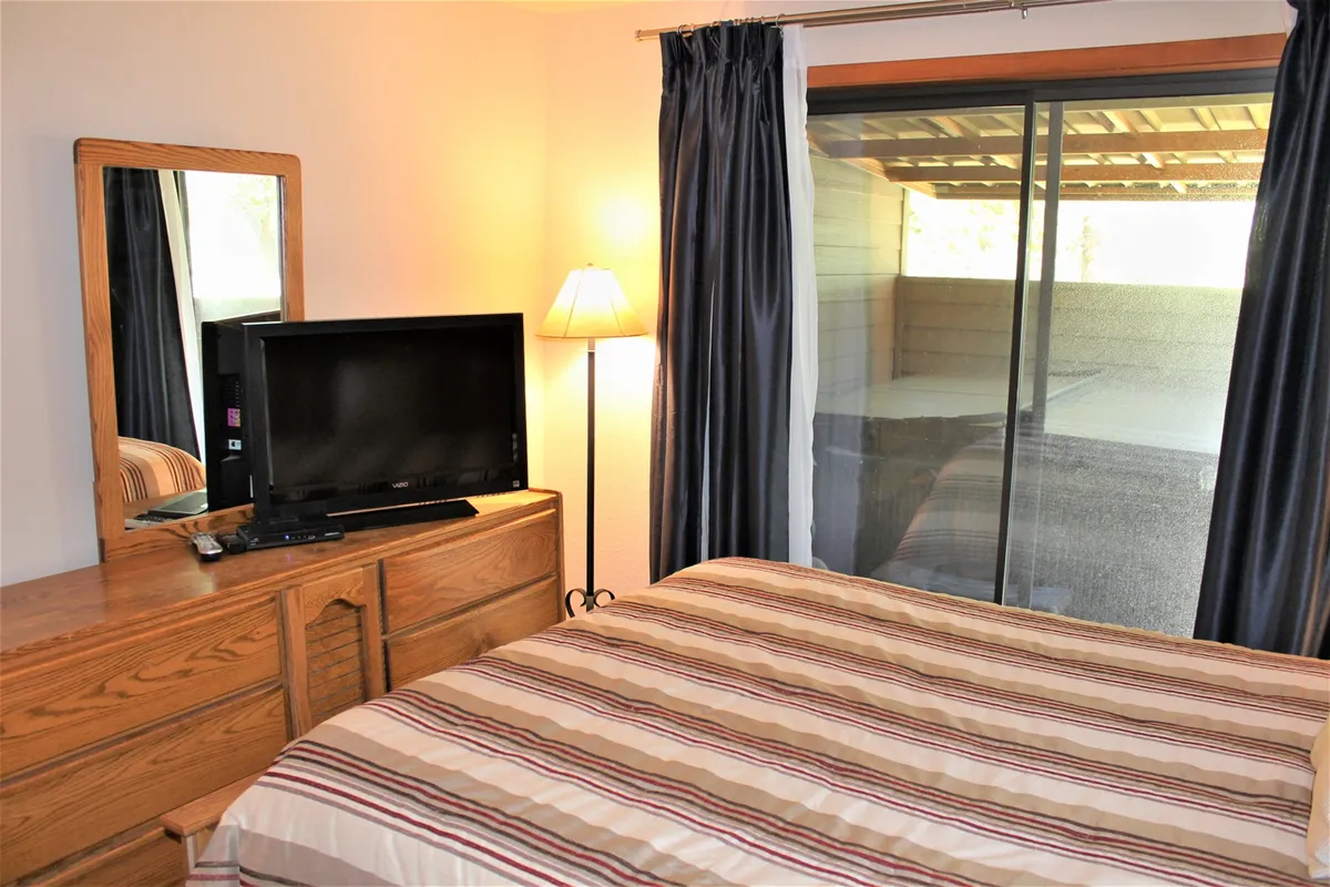 A cozy bedroom with a striped bedding set, TV mounted opposite the bed, and warm lighting from a bedside lamp. The space feels welcoming, ideal for unwinding after a long day.