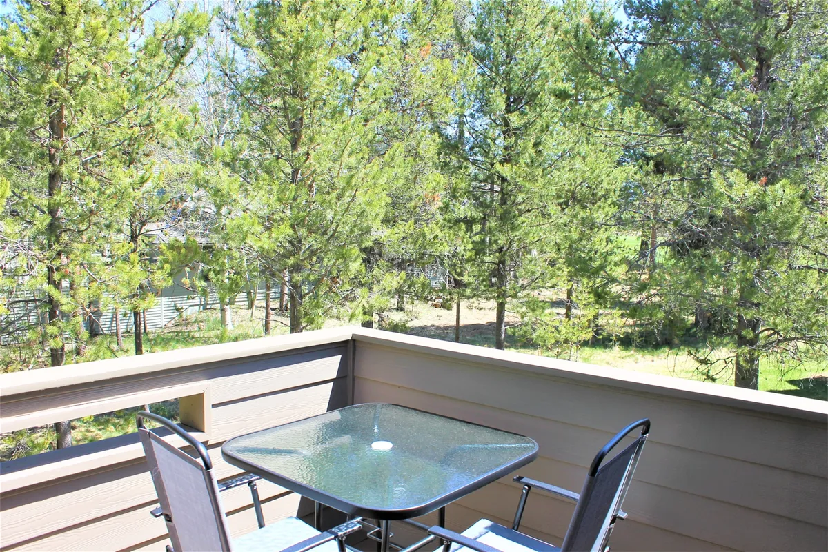 An outdoor dining area with a glass table, metal chairs, and lush green trees surrounding the space. The setting suggests a tranquil spot for enjoying meals, games, or simply relaxing after a day of adventure.